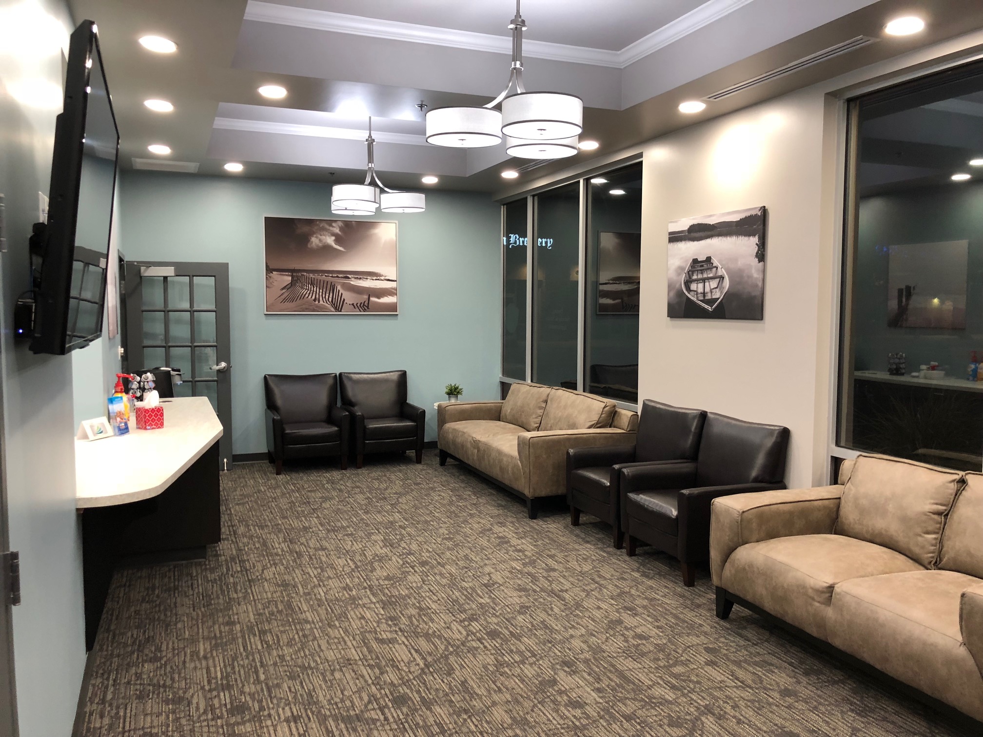 Modern waiting room with beige armchairs, a reception desk, hanging lights, and framed black and white photographs on the walls | Pleasant Dental