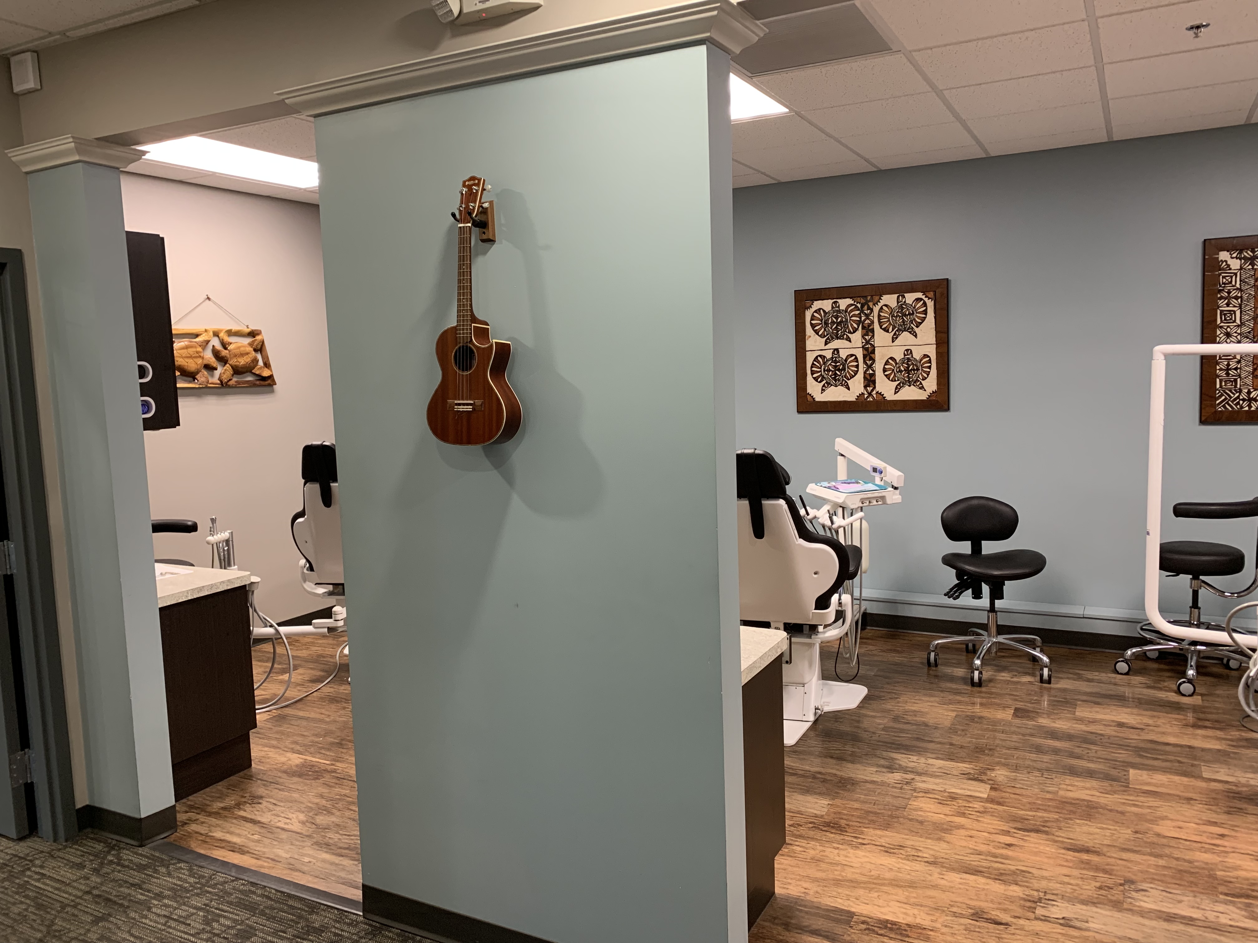 A ukulele hangs on a light green column in a modern dental office, contrasting with the clinical setting marked by dental chairs and equipment in the background | Pleasant Dental