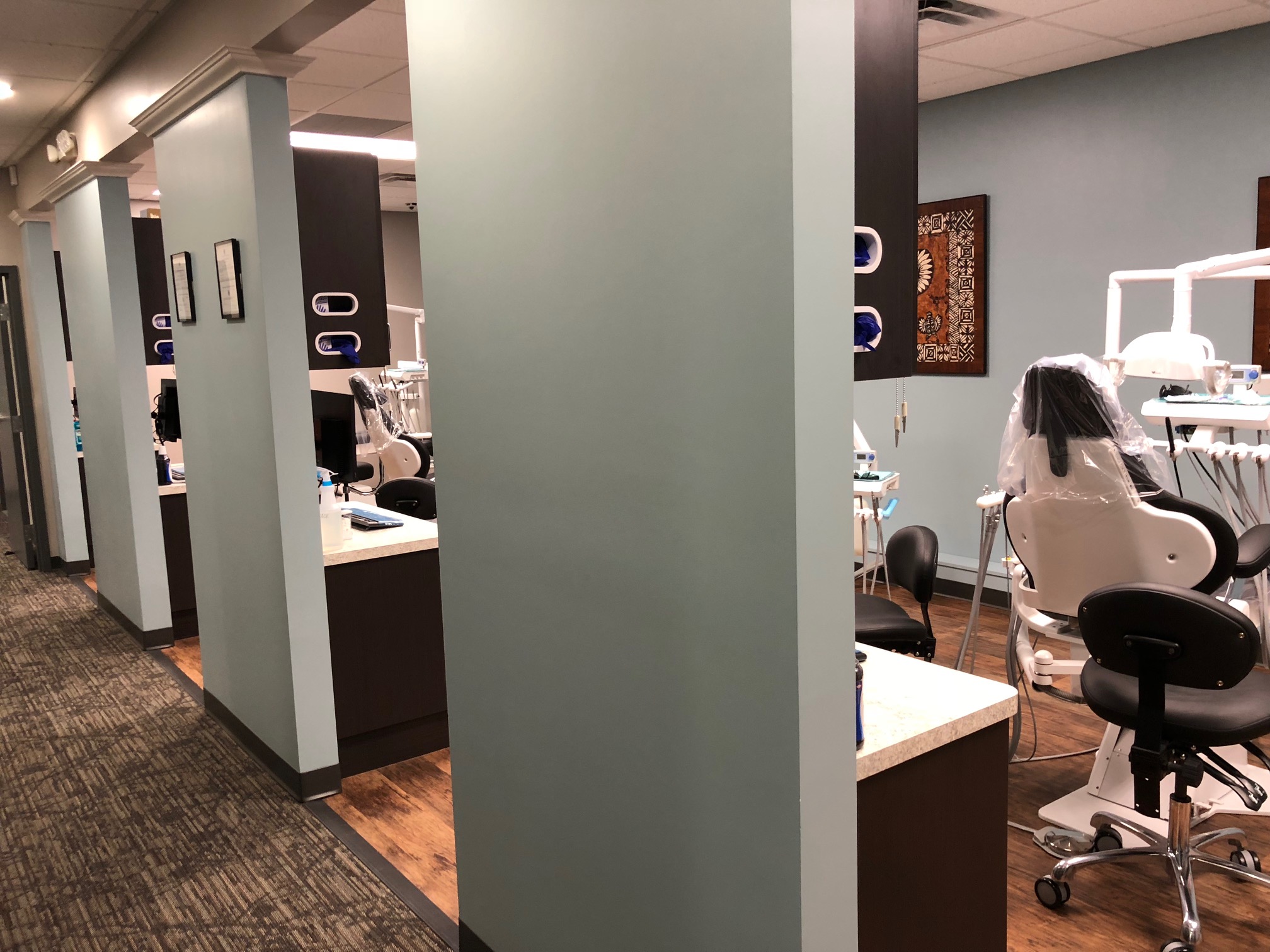 Modern hair salon interior featuring a row of styling stations with mirrors, chairs, and counters, set against a muted color palette. decorative elements and clean layout visible | Pleasant Dental
